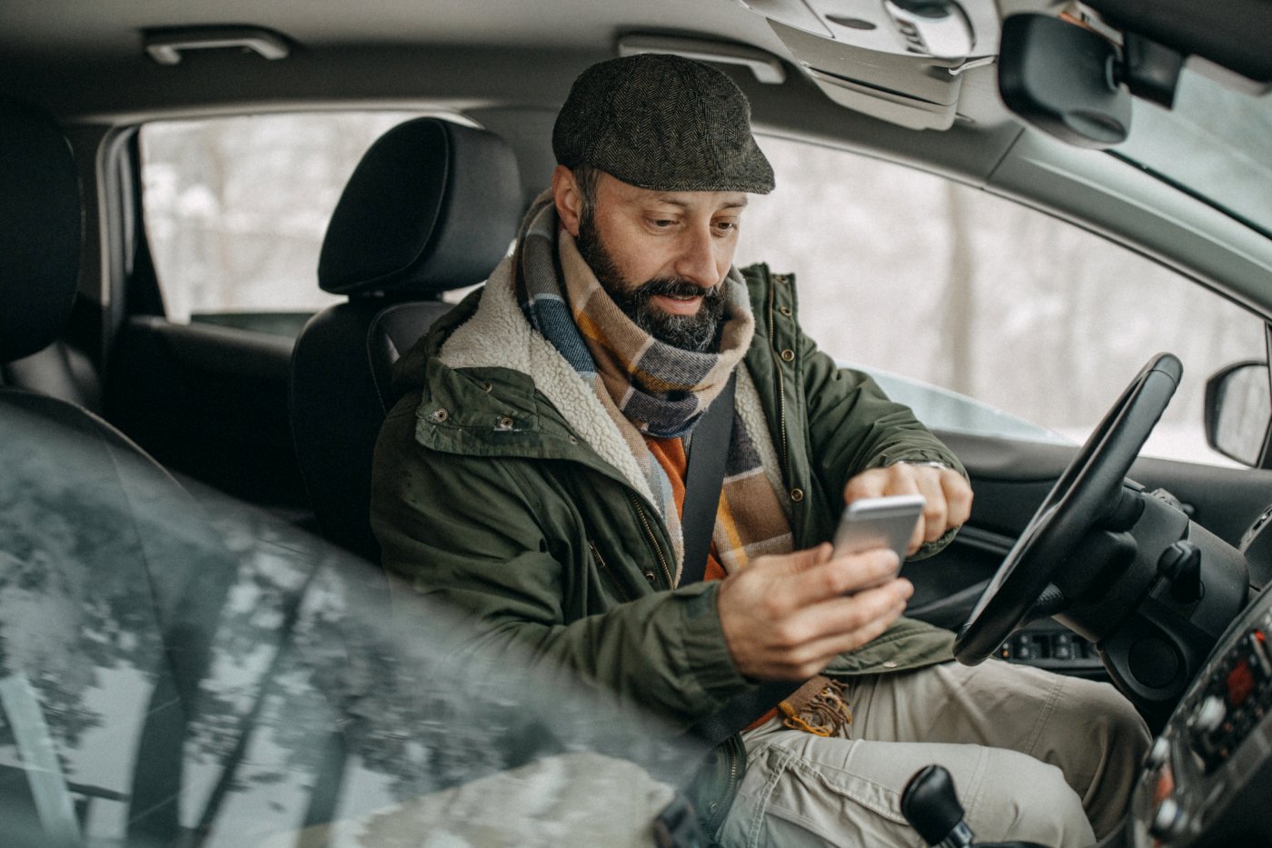 en mann med hatt og jakke sitter i bilen og taster på mobilen