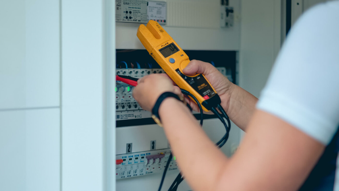 elektriker monterer nytt sikringsskap med automatsikringer, med bruk av gult verktøy tilkoblet sikringsskap.