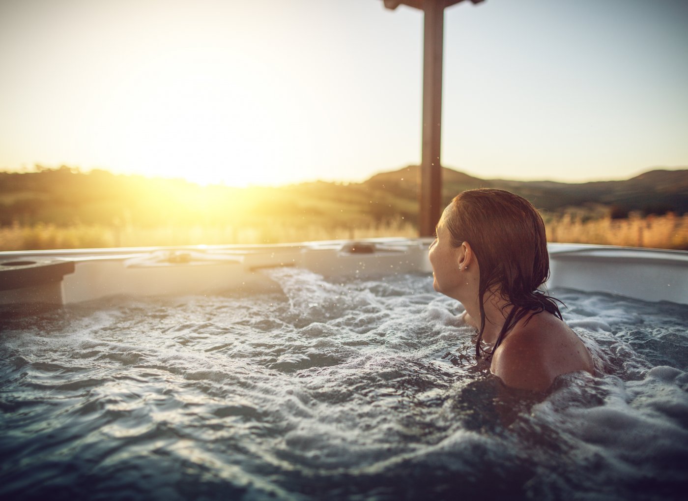 kvinne sitter i boblende bad og ser på nedadgående sol