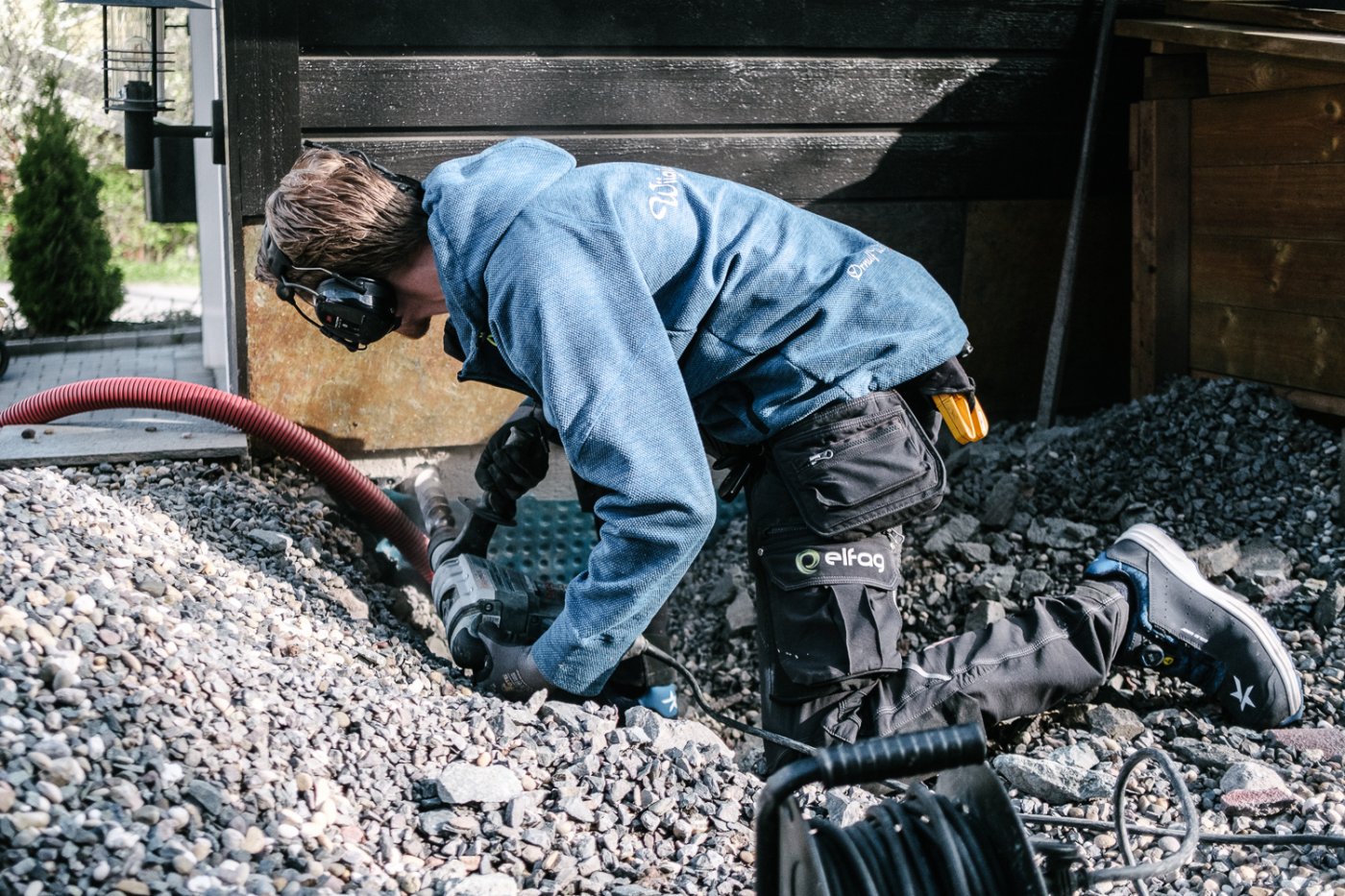 Elektriker Fredrik ligger på alle fire og trekker kabler under bakken og til ladeboks.