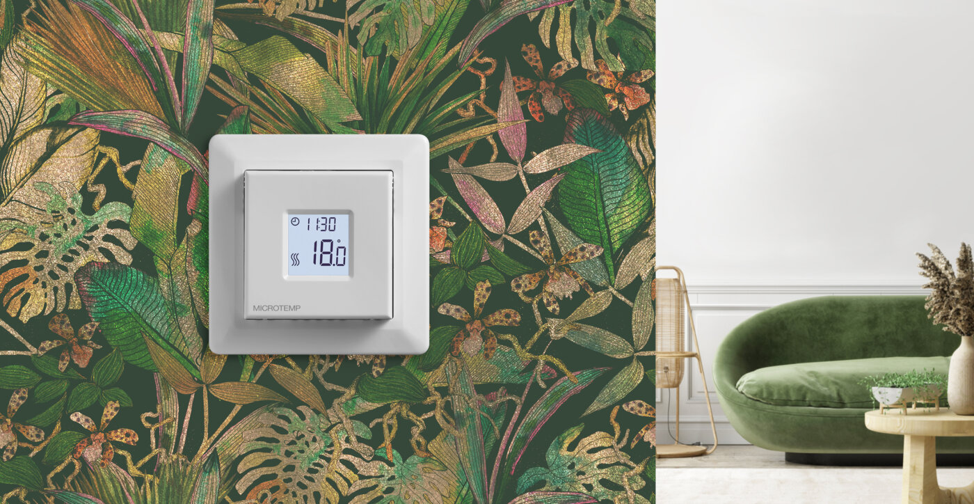 Hvit termostat med 18 grader i displayet, Montert på vegg med grønn tapet.