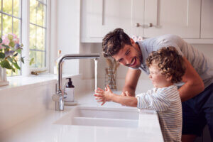 Far og lite barn vasker hender under kran med rennende vann.